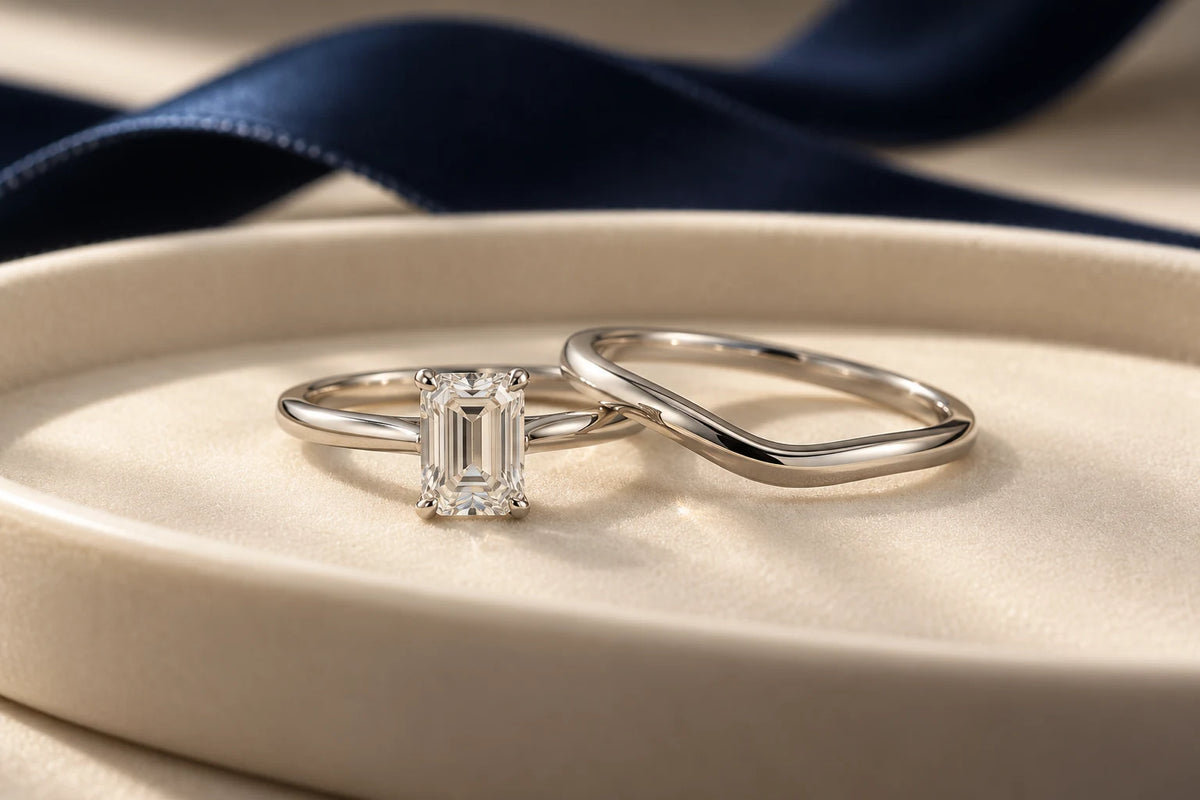 Concept of an emerald-cut solitaire and curved platinum-appearance band on an ivory tray